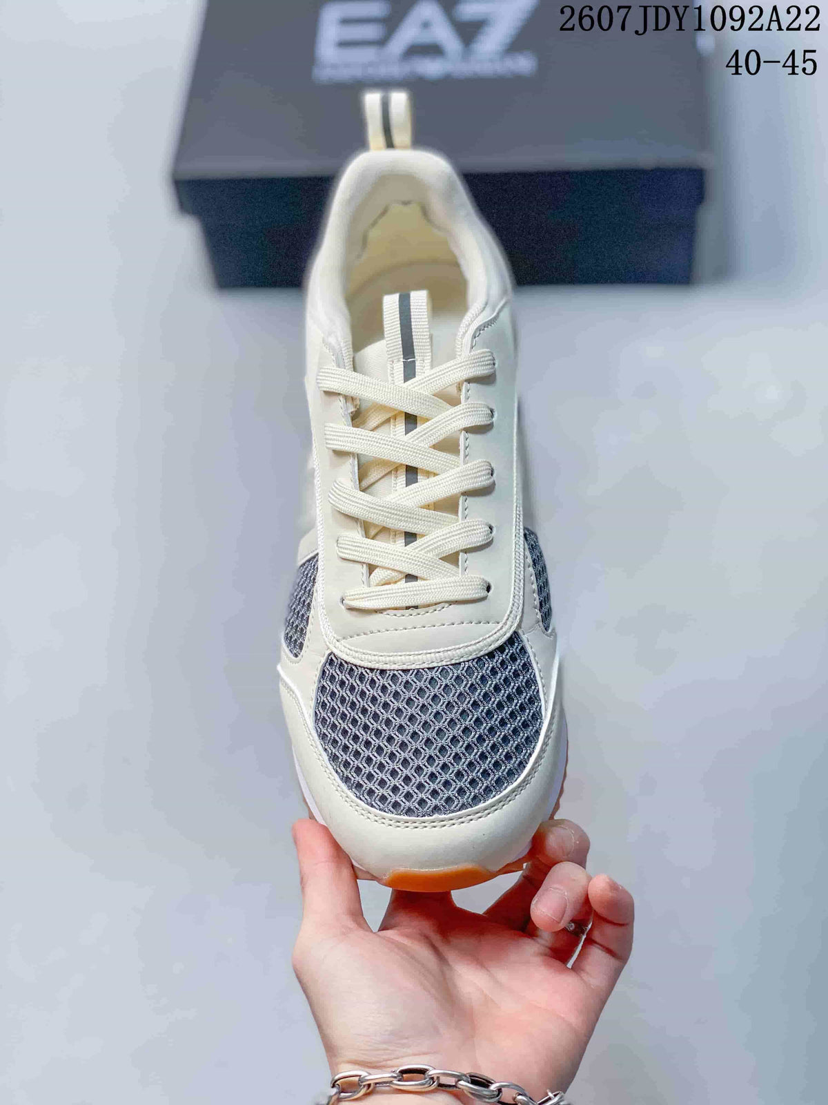 Top view of an EA7 sneaker showing cream laces, gray patterned mesh at the toe, and an off-white upper.