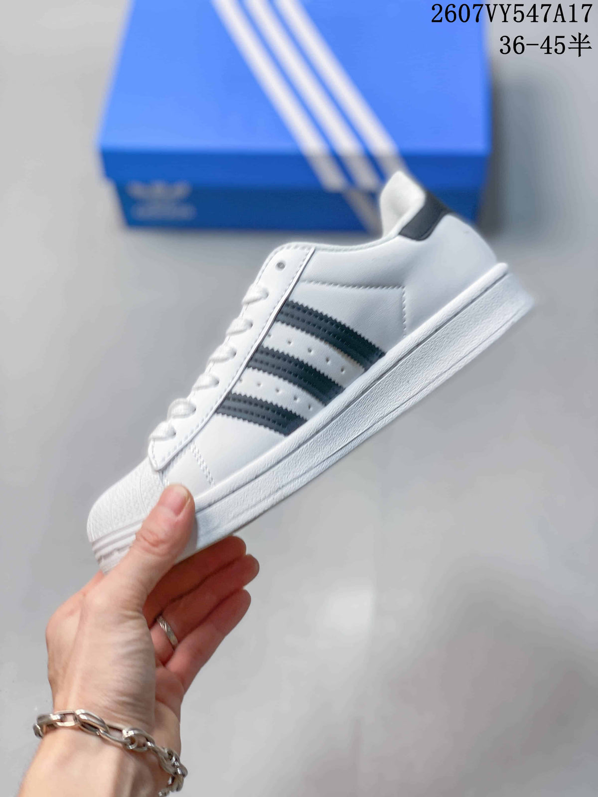 Side profile of the white low-top sneaker showing black three-stripe details, perforations, laces, and a textured shell-style toe.