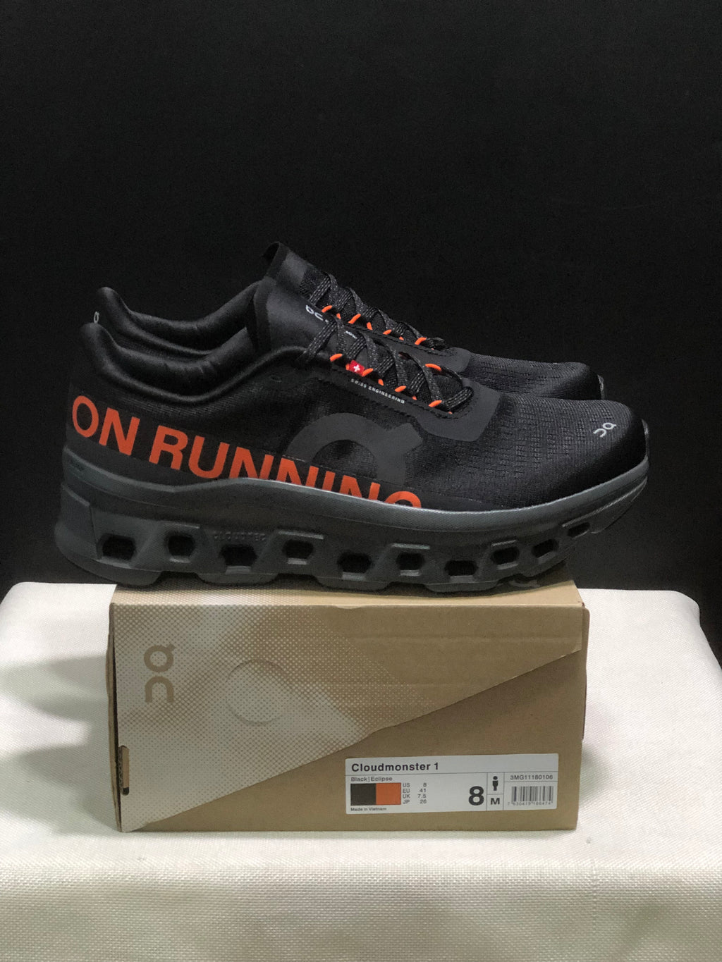 Side view of black Cloudmonster 1 sneakers with orange side lettering and a sculpted dark outsole.