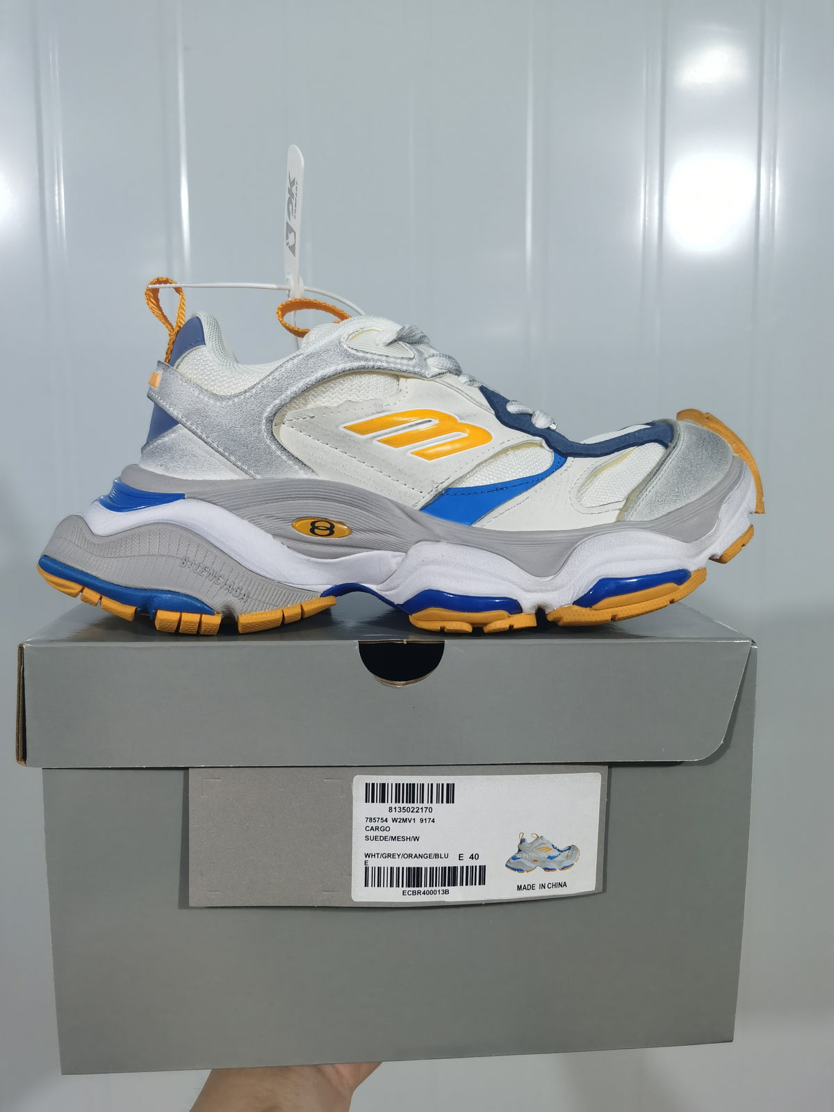 Side view of a New Balance 9174 sneaker displayed above its box; the box label shows EU size 40 and the color text WHT/GREY/ORANGE/BLU.