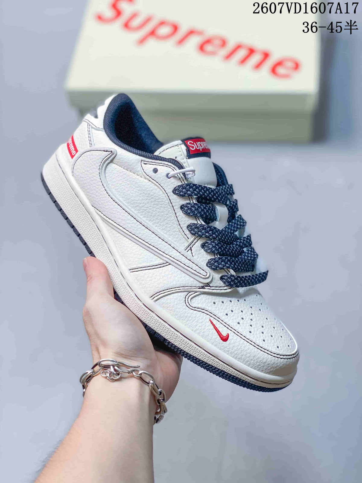 White low-top sneaker with dark laces, outlined side overlay, red swoosh-style mark and a red-and-white branded box in the background.