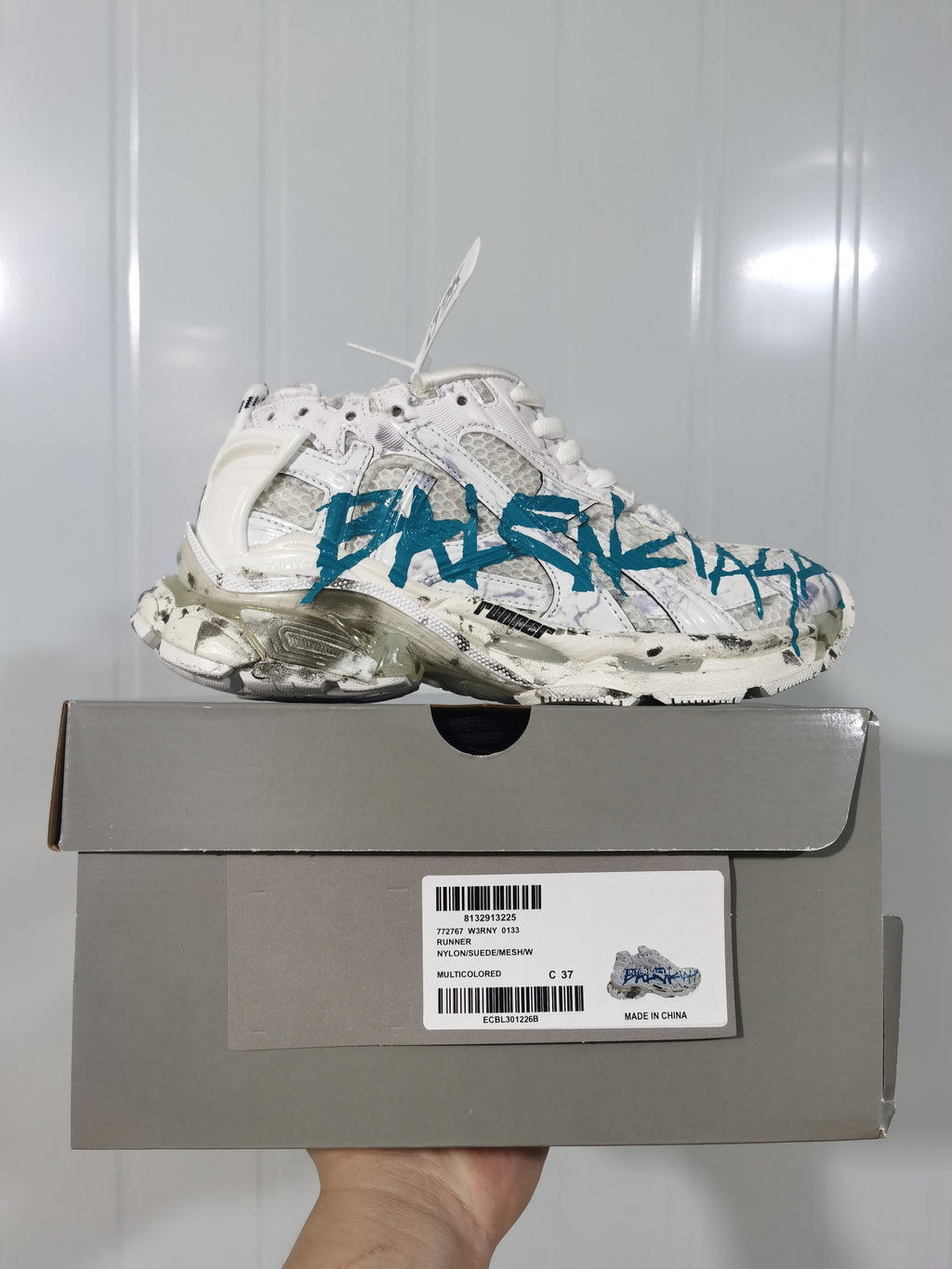 Side view of a white and blue Runner sneaker displayed on its box; the box label shows model code 0133, color description Multicolored, and Made in China.