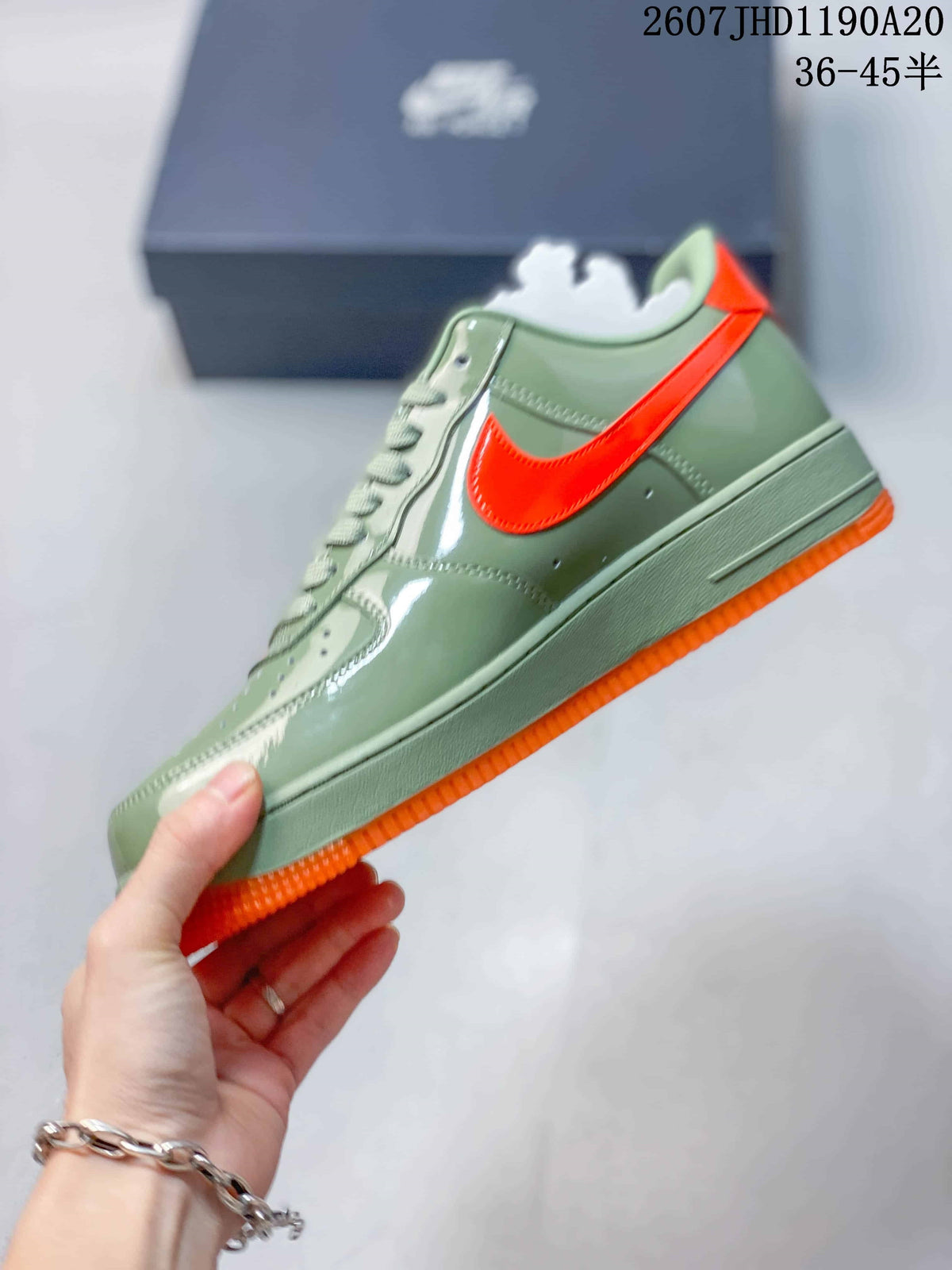 Side view showing the green upper, bright orange Swoosh-style branding, stitching, and orange outsole.