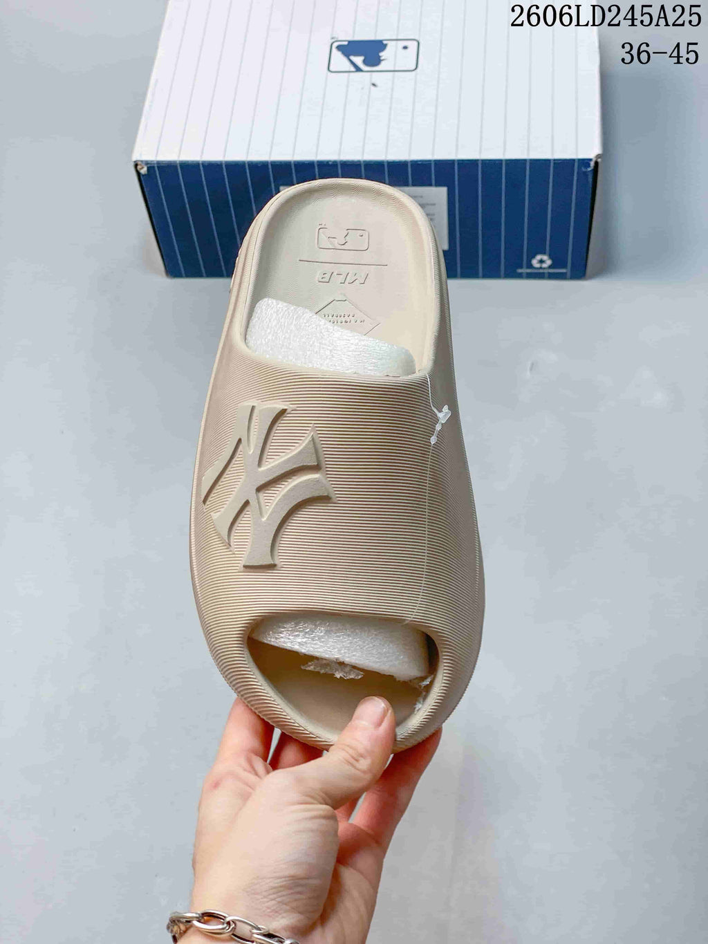 Top view of a beige MLB slide sandal showing the open toe, wide logo strap, and textured surface.