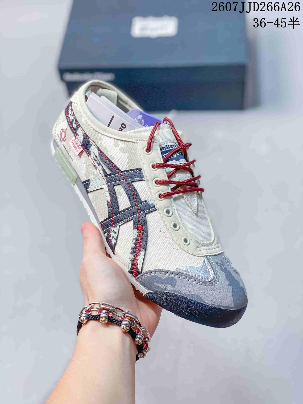 Angled side view of the sneaker showing the cream upper, navy stripes, red stitching, side tags, and gray patterned toe panel.