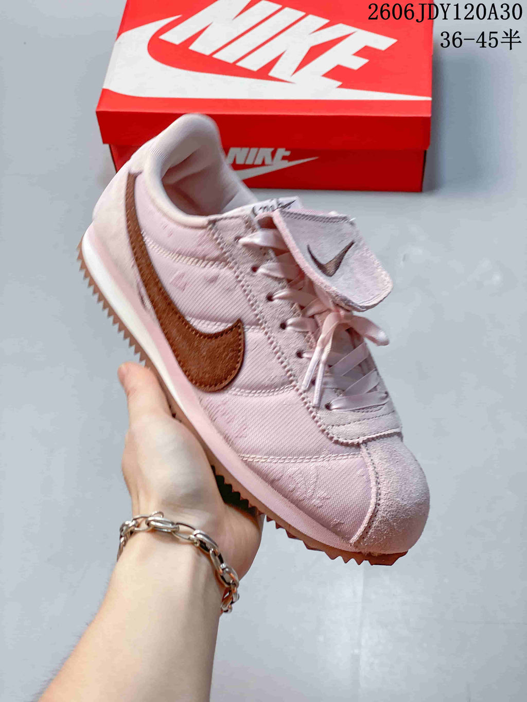 Angled side view of a pale pink Nike Classic Cortez sneaker with brown accents