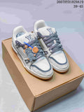 Pair of white and gray Louis Vuitton Trainer Maxi sneakers displayed on a cardboard box, with gray laces, decorative lace accessories, and the visible code 2607HYD1829A19.