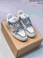 Pair of white and gray Louis Vuitton Trainer Maxi sneakers displayed on a cardboard box, with gray laces, decorative lace accessories, and the visible code 2607HYD1829A19.