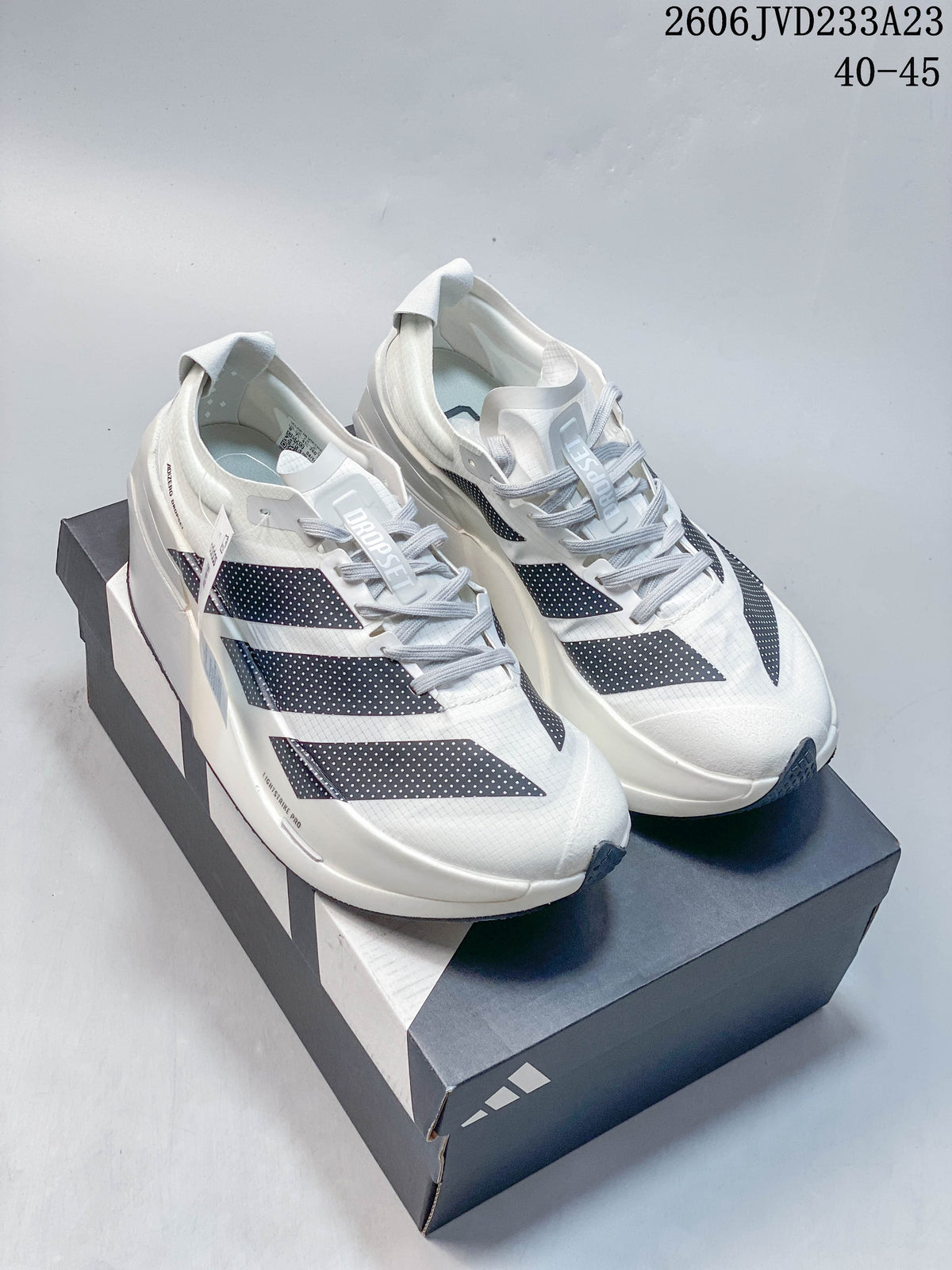 Pair of white Adidas Adizero Prime X3 running shoes with navy dotted stripes on a branded box