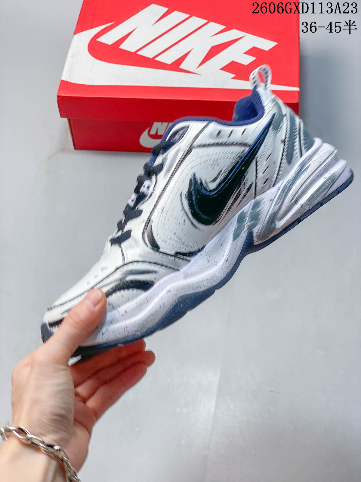 Side view of a white Nike Air Monarch IV sneaker with navy accents and layered panels.