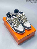 Pair of low-top sneakers in navy, cream, and olive tones displayed on an orange shoebox, with multiple lace elements and a perforated toe box.