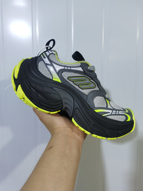 Close-up side view of a grey, black and bright yellow chunky lace-up sneaker with layered panels and a thick black outsole.