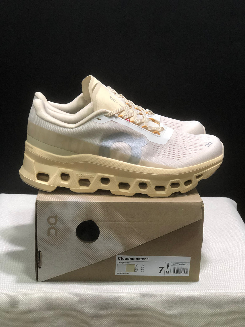 Side view of the cream and white On Cloudmonster 1 sneakers showing the padded collar and sculpted midsole.