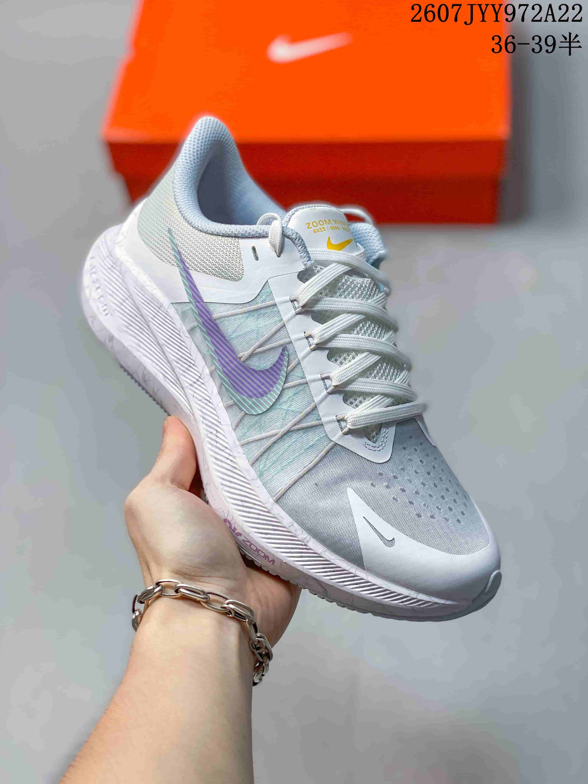 Angled close-up of a light gray Nike Air Zoom Winflo 8 shoe with purple and teal side accents, mesh-style upper, and textured midsole.