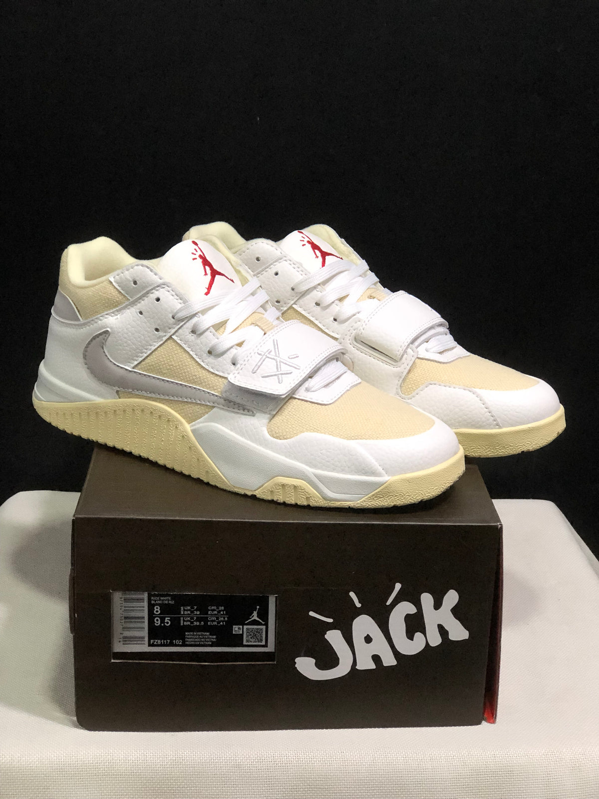 Front three-quarter view of the white and cream sneakers showing the laces, midfoot straps and red tongue branding.