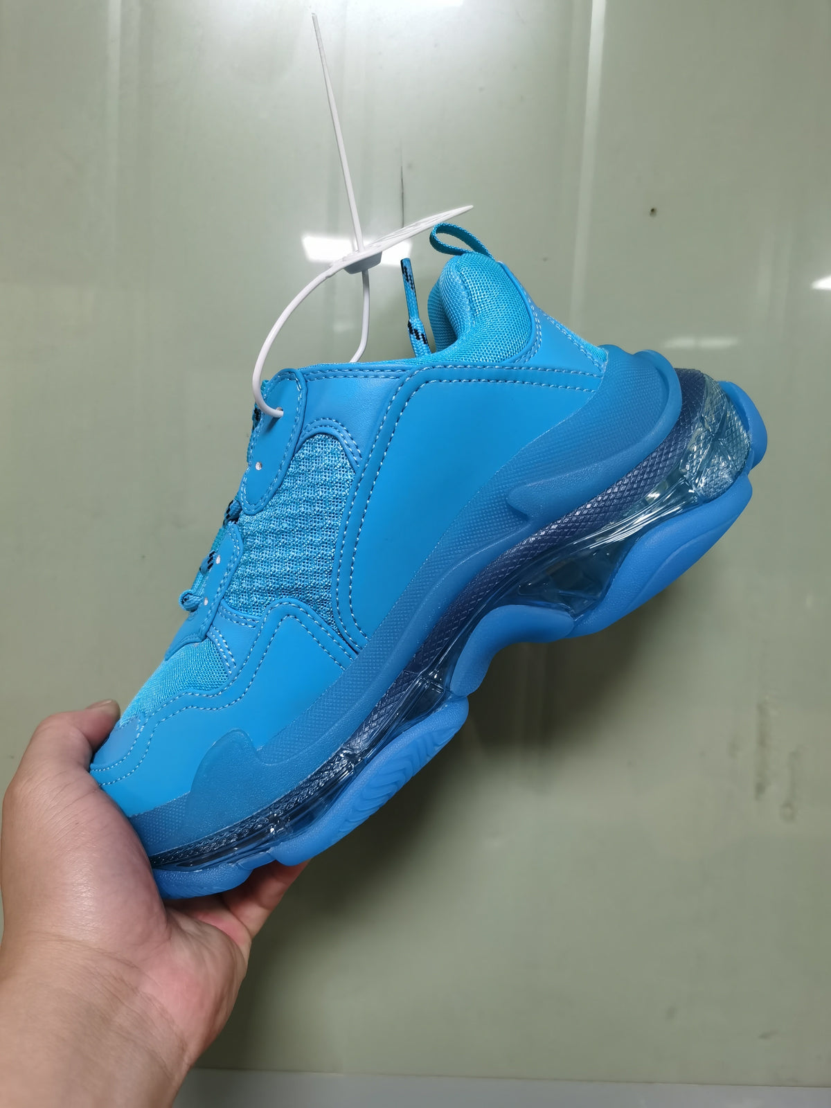 Close-up side view of a cyan blue Balenciaga sneaker showing mesh panels, tonal stitching, and a layered clear-look sole.