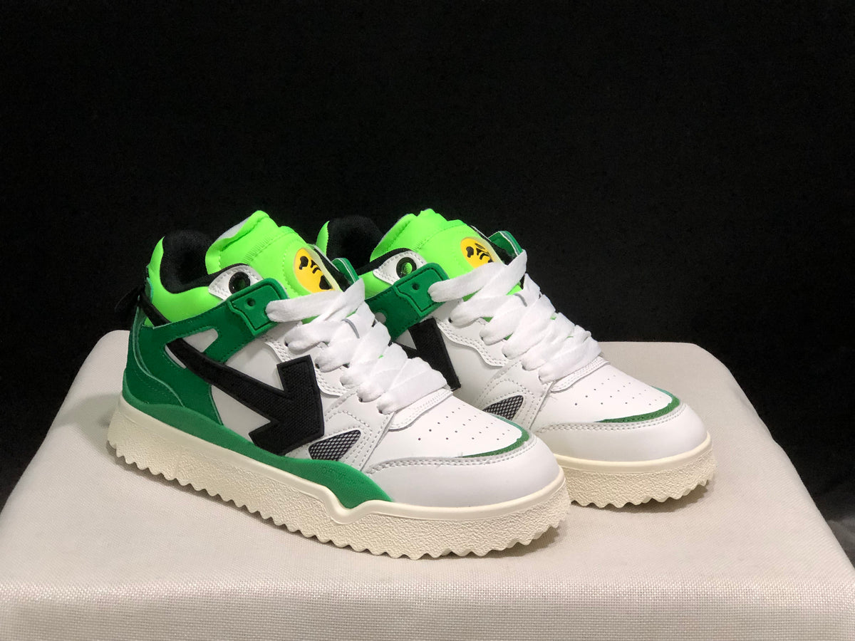 Three-quarter front view highlighting the white uppers, green overlays, black side arrows, and cream outsoles.