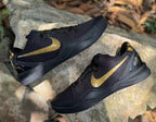 Angled view of the black and gold sneaker pair with gold Swooshes and heel graphics visible.