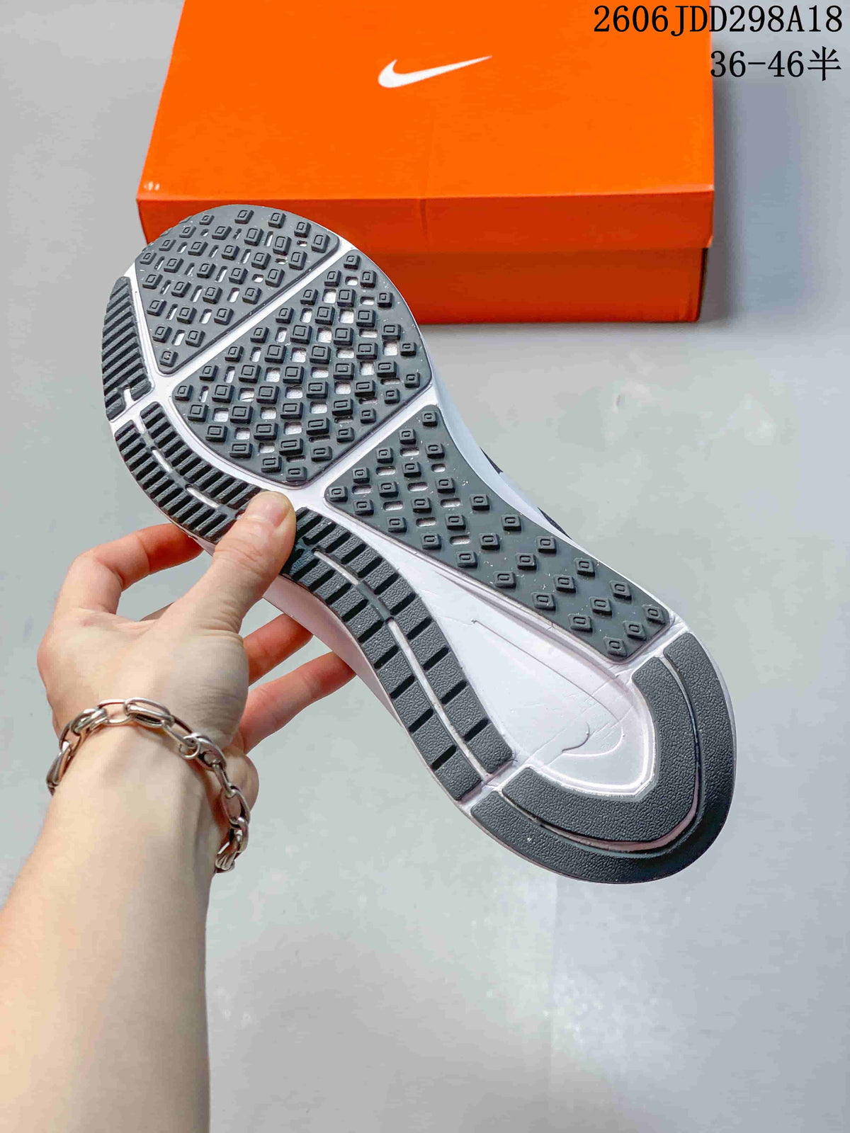 Underside view of a gray Nike sneaker showing the patterned rubber outsole and orange Nike shoebox.