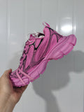 Close-up side view of a pink Nike sneaker with black outlined panels, pink laces, and a segmented textured outsole.