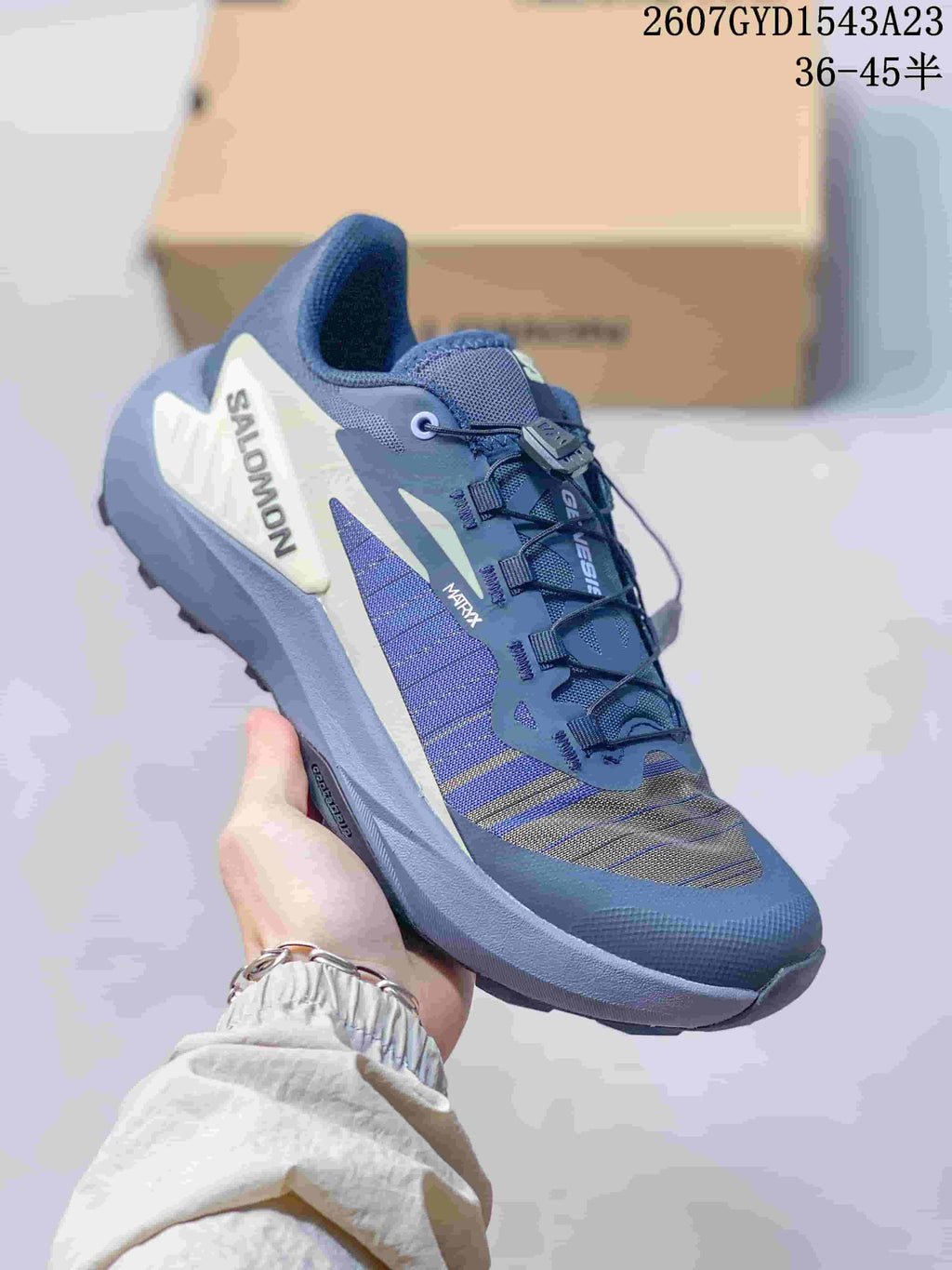 Blue and gray Salomon Genesis trail shoe held at an angle, with visible model lettering and outdoor tread.