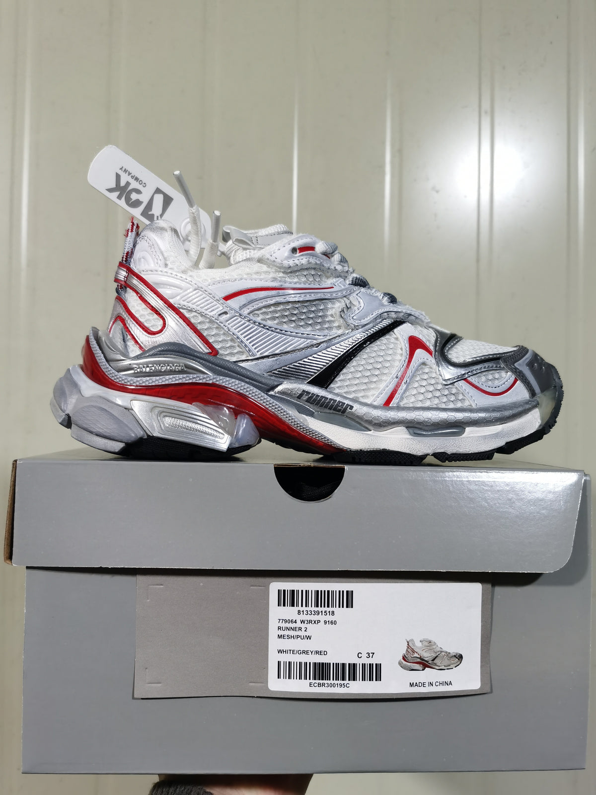 Side profile of the sneaker displayed on its box; the box label identifies 9160 Runner 2, White/Grey/Red, and size C 37.