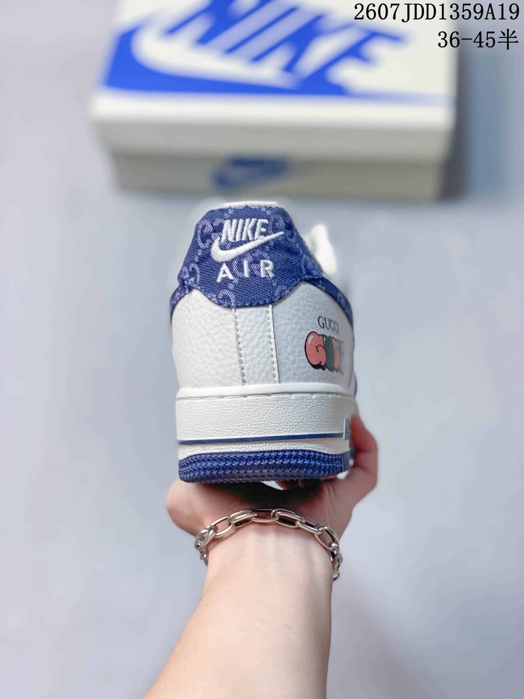 Rear view of a white and blue sneaker showing the heel panel, blue outsole edge, and decorative side lettering.