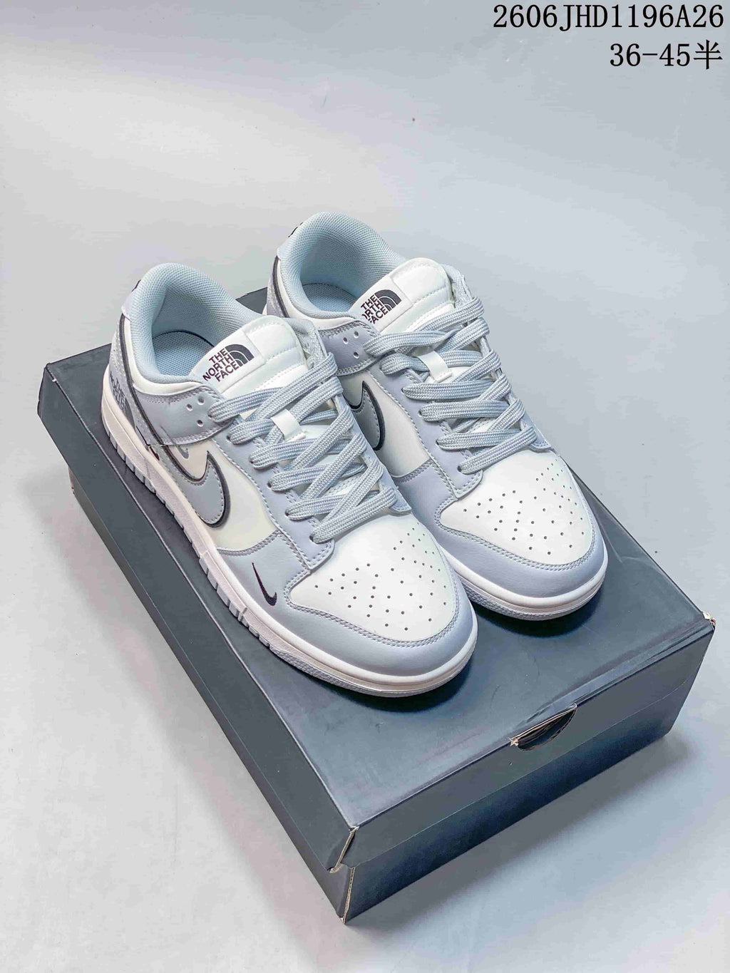 Pair of white and light gray low-top sneakers with perforated toes and contrasting Swoosh details, shown on a box.