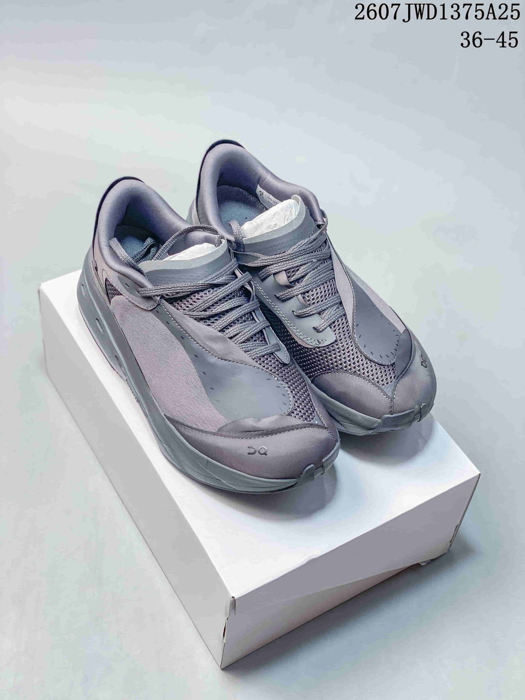 Pair of gray On sneakers displayed on a white box, showing the layered upper, mesh panels, laces, and padded collars.