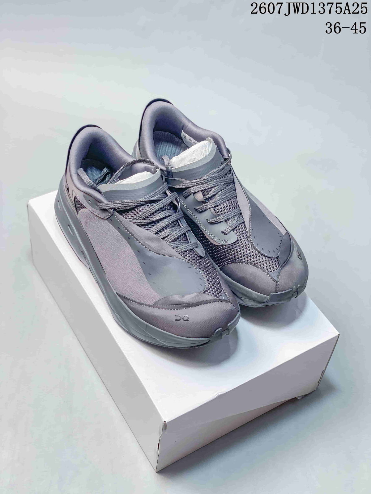 Pair of gray On sneakers displayed on a white box, showing the layered upper, mesh panels, laces, and padded collars.
