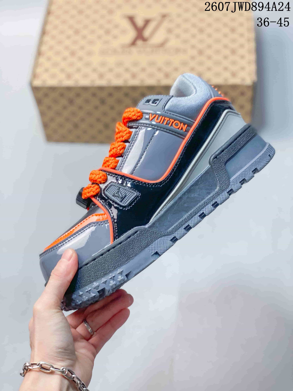 Side view showing the gray low-top sneaker, glossy black overlays, orange trim, and chunky treaded sole.