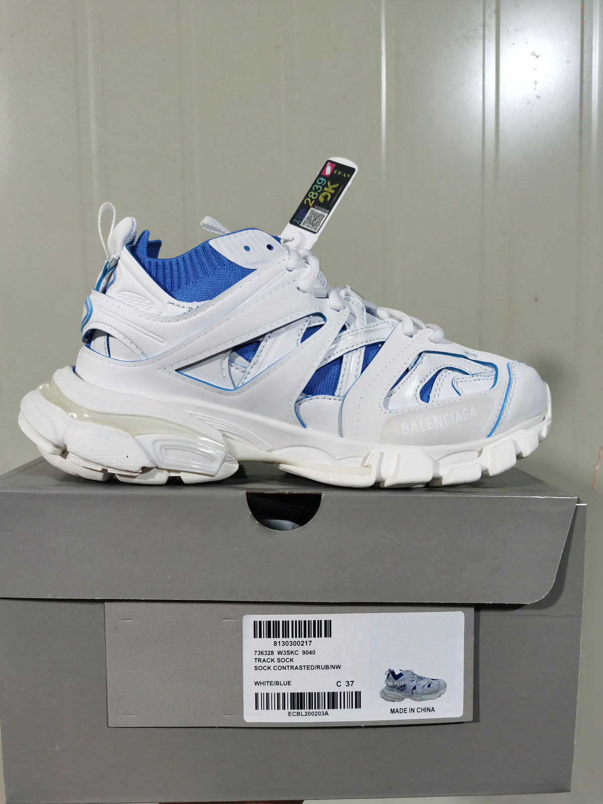 Side view of a white and blue Balenciaga Track Sock sneaker resting on its box; the label shows Track Sock, code 9040, color White/Blue and size C 37.