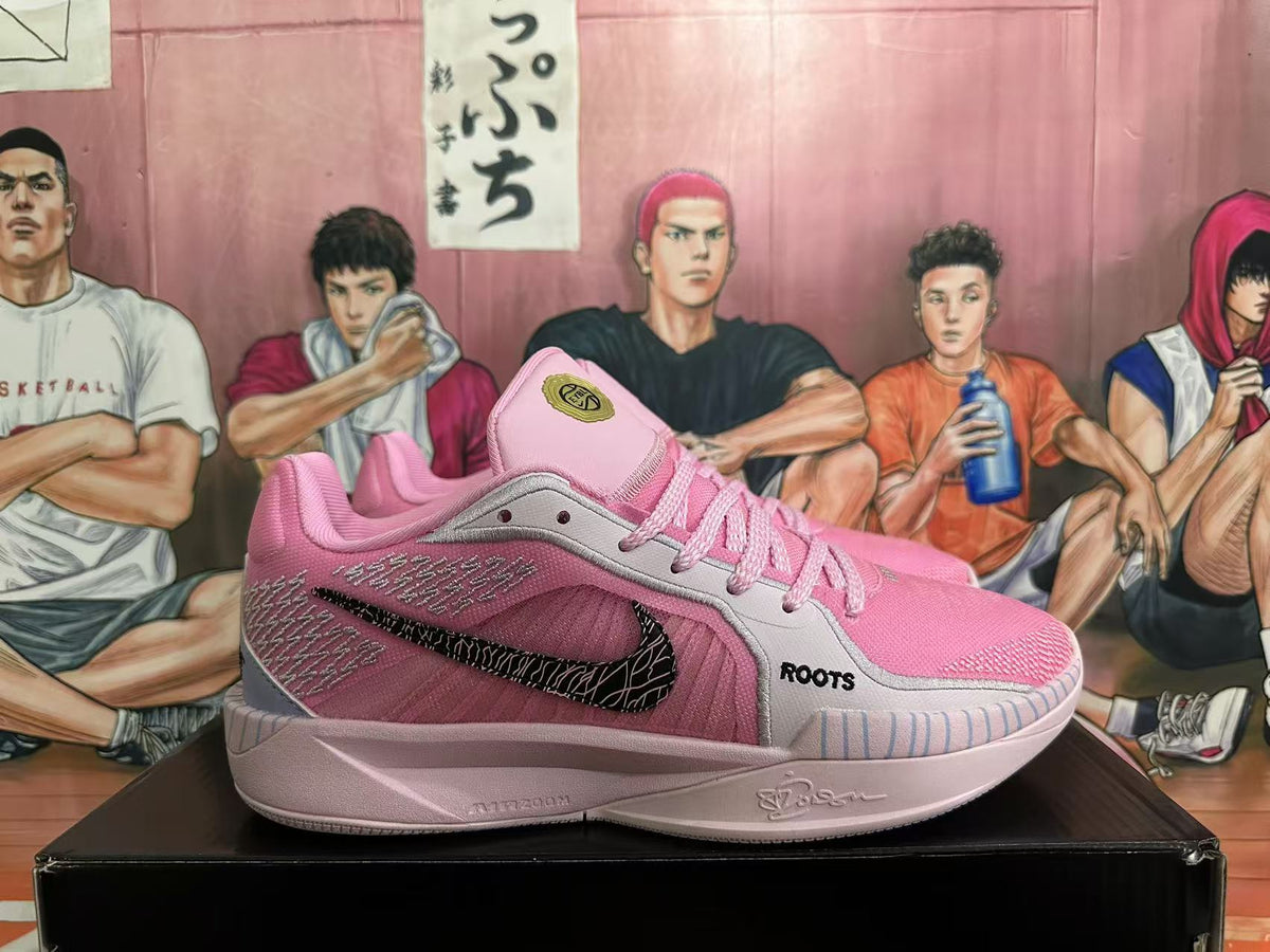 Side view of a pink basketball shoe with gray panels, a black patterned Swoosh, and ROOTS lettering.