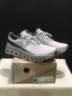 Pair of light gray and white On Cloudmonster 1 sneakers displayed on their shoebox; the box label identifies Glacier | Alloy and a photographed EU 41 sample.