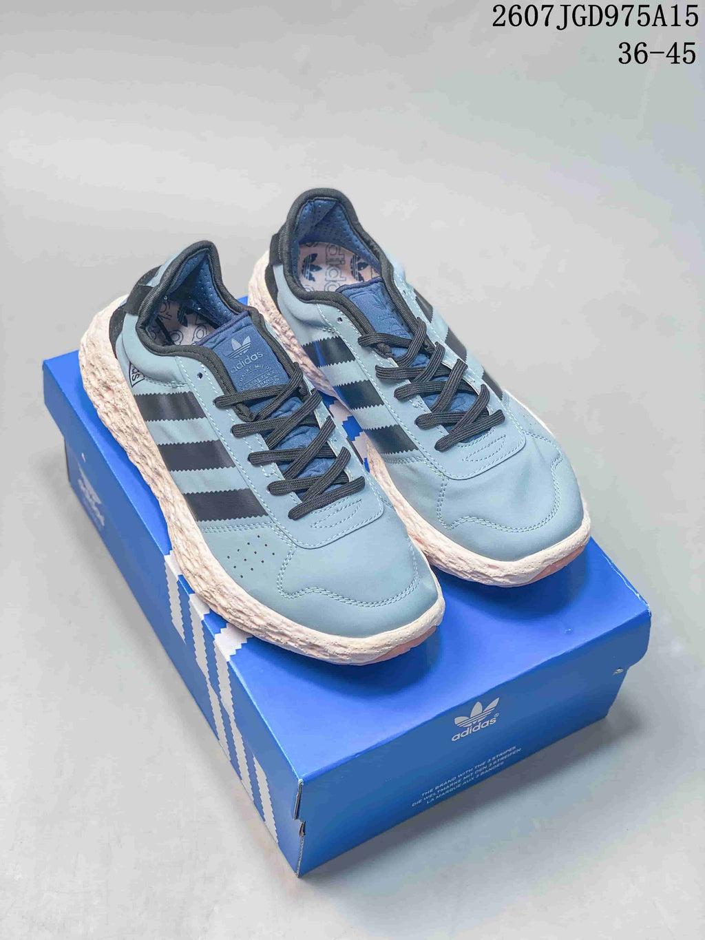 Pair of light blue Adidas Originals low-top sneakers with black stripes, cream textured midsoles, and a blue shoe box.