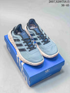 Pair of light blue Adidas Originals low-top sneakers with black stripes, cream textured midsoles, and a blue shoe box.