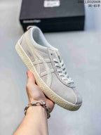 Angled side view of the light gray ASICS Japan S sneaker showing the side branding, layered stripes, laces, and textured outsole.