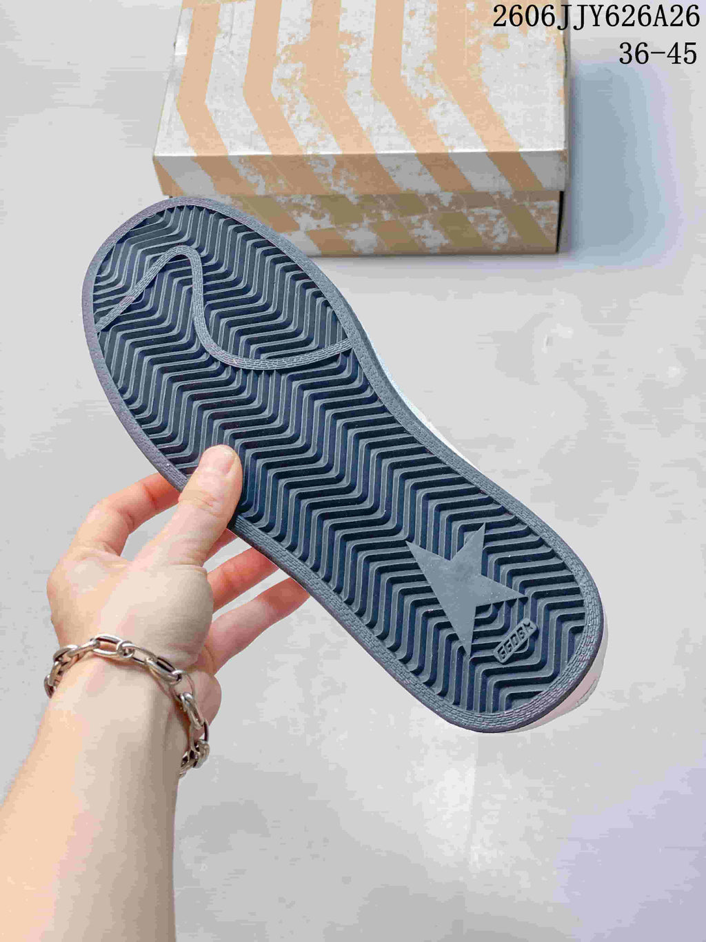 Close-up of the sneaker outsole showing a dark zigzag tread pattern and embossed branding.