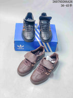 Black and brown adidas Originals Samba sneakers shown together from above on a blue shoebox, highlighting the two colorways and flap tongues.