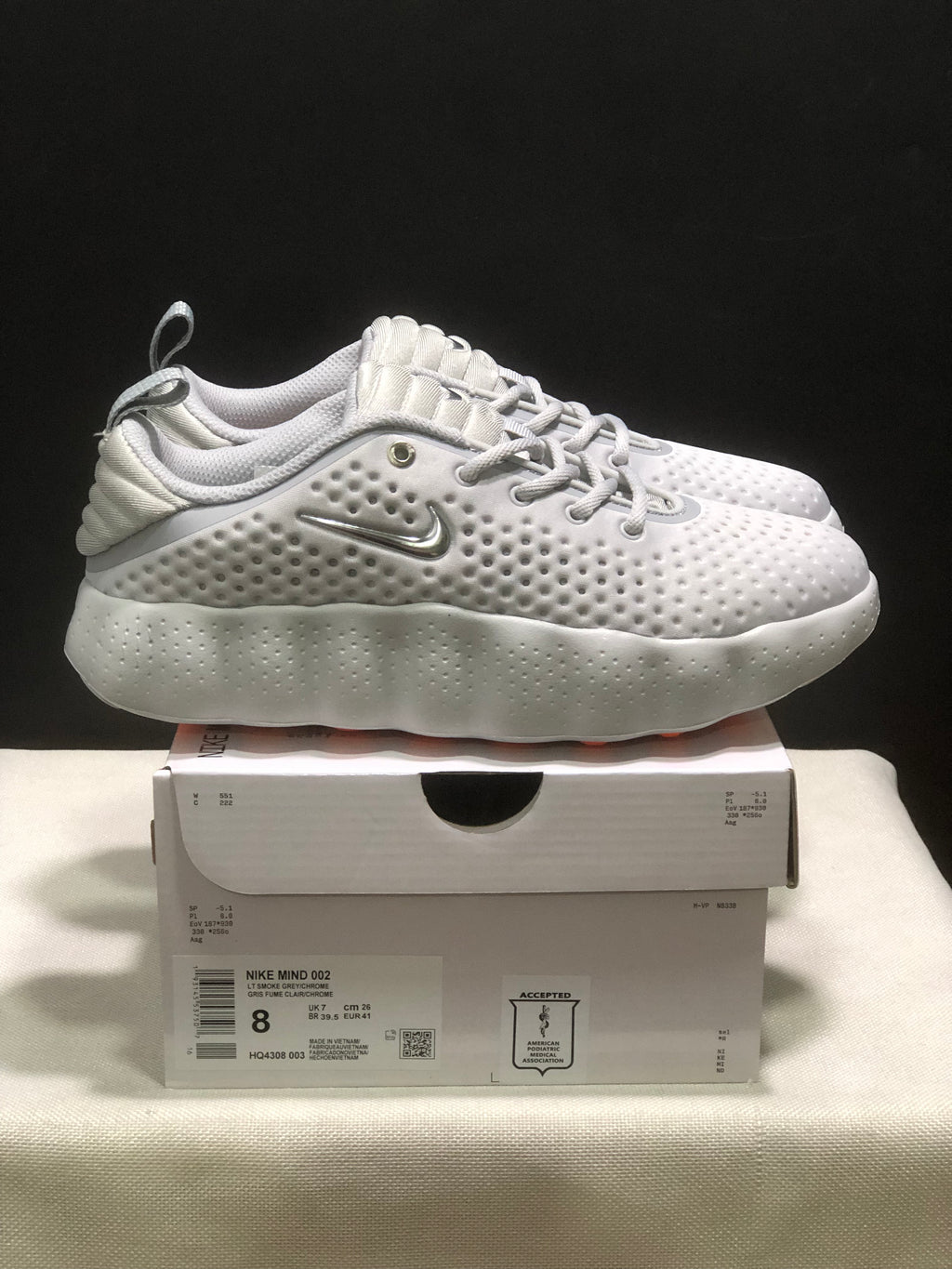 Side view of white Nike Mind 002 sneakers with textured uppers, lace-up fronts and sculpted midsoles.