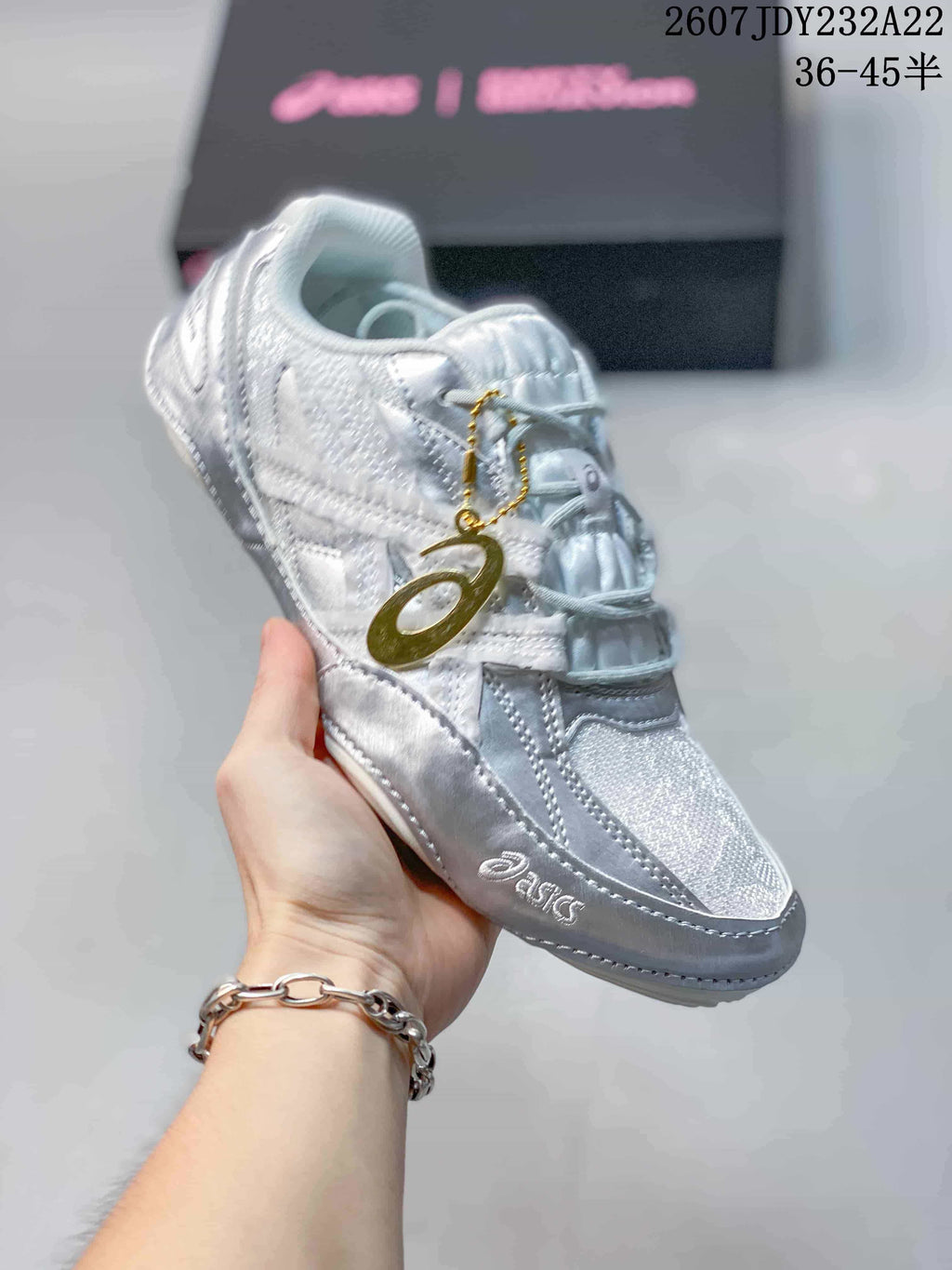 Three-quarter view of the silver and white ASICS sneaker showing the layered upper, padded tongue, side branding, and lace charm.
