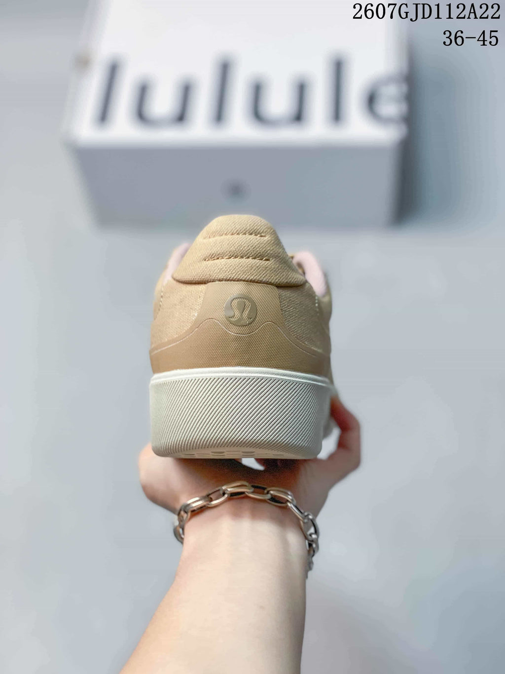 Rear view of the tan sneaker showing the padded heel, circular logo detail and light-colored outsole.