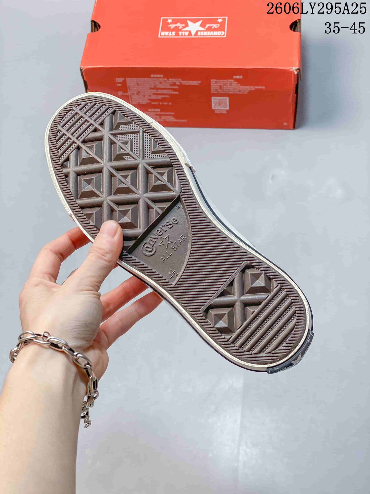 Outsole view of a Converse sneaker showing the textured tread pattern and Converse All Star branding, with the shoebox in the background.