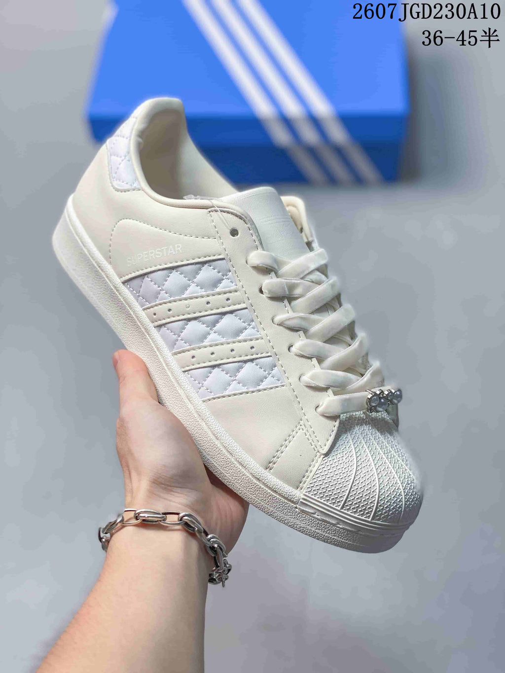 Angled side view of the white Adidas Superstar sneaker showing the shell toe, quilted stripe panel, and Superstar side text.