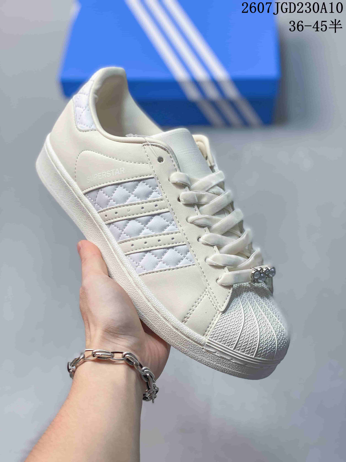 Angled side view of the white Adidas Superstar sneaker showing the shell toe, quilted stripe panel, and Superstar side text.