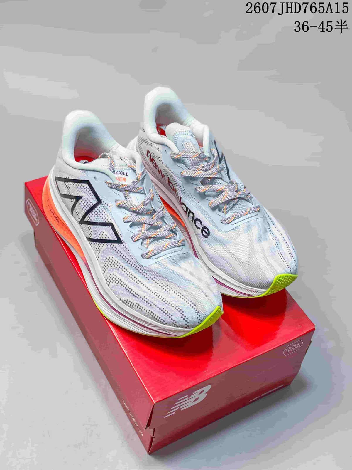 Pair of light-colored New Balance RC Elite running shoes displayed on a red shoebox, with orange and lime outsole accents.