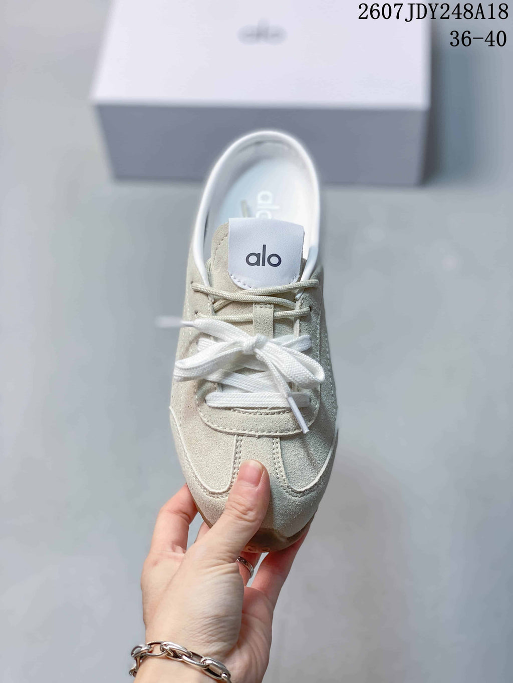Top view of a cream Alo sneaker showing the tongue logo, white laces, and stitched upper panels.