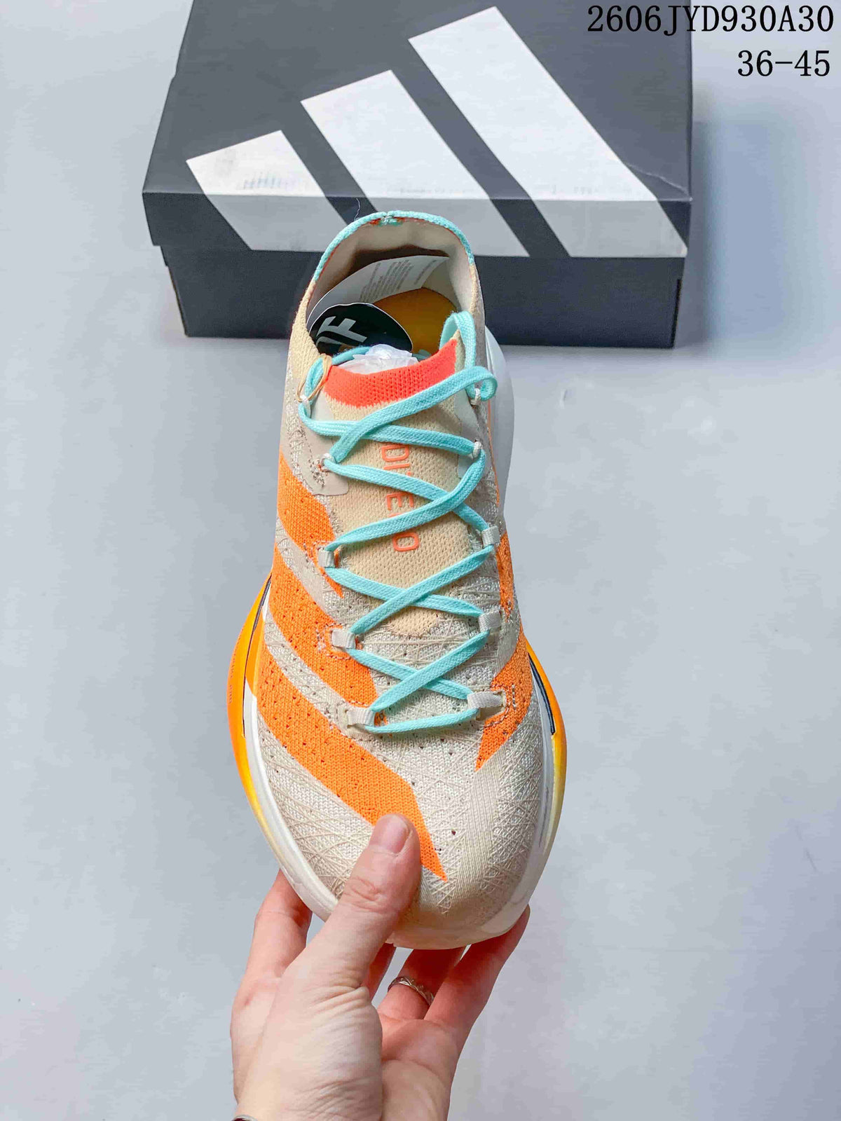 Front view of a beige running shoe with orange stripes and turquoise laces