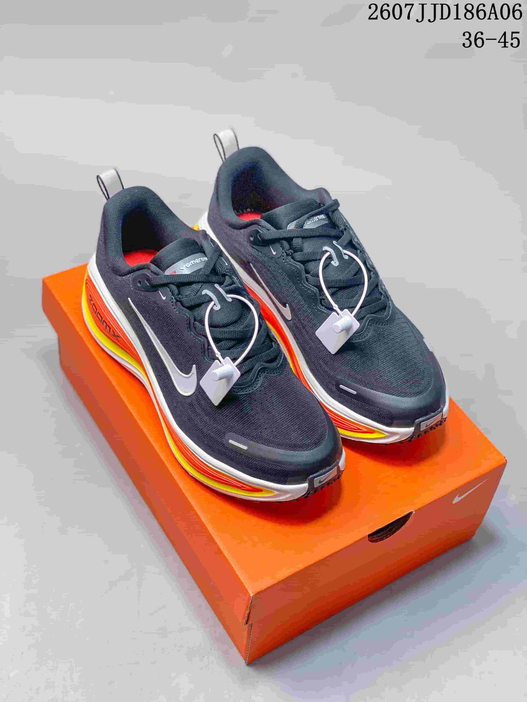 Pair of dark Nike Vomero 18 GTX running shoes displayed on an orange shoebox, showing white swooshes and bright orange and yellow midsole accents.