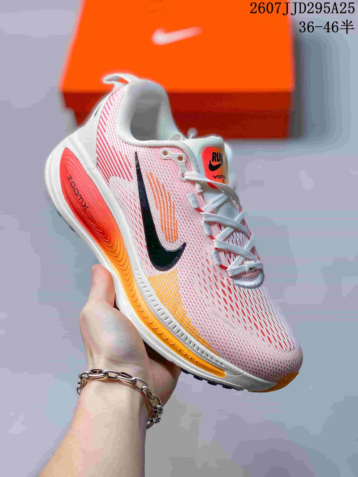 Close side view of a Nike Vomero 18 sneaker showing the pink and white upper, black Swoosh, orange midsole accents, and orange outsole detail.